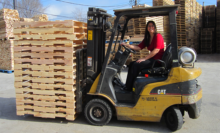 woman on machine moving wooden pallets